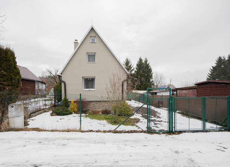 Ein Haus in Handlová mit etwas Schnee im Hof, umgeben von Grün und einem Zaun.
