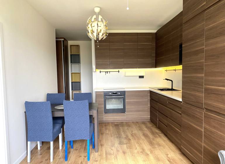 Küche in einer 3-Zimmer-Wohnung mit Esstisch, moderner Beleuchtung und Boden mit Holzdekor.