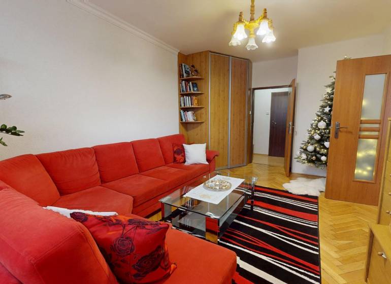 Wohnzimmer in einer 3-Zimmer-Wohnung mit rotem Sofa, Tannenbaum und Holzboden.