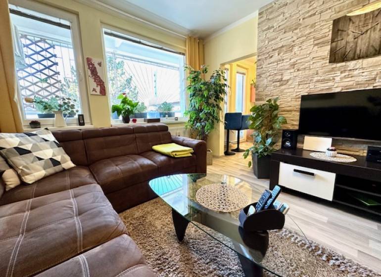 Wohnzimmer in einer Einzimmerwohnung mit braunem Sofa und Boden in Holzoptik.