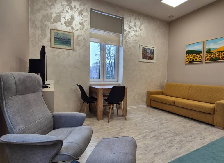 Wohnzimmer einer Einzimmerwohnung mit Sessel, Sofa und Tisch, Boden mit Holzdekor.