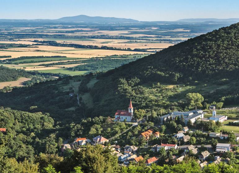 Panoramablick auf ein Dorf im Tal, umgeben von Wäldern und Feldern. Grundstücke geeignet zum Wohnen.