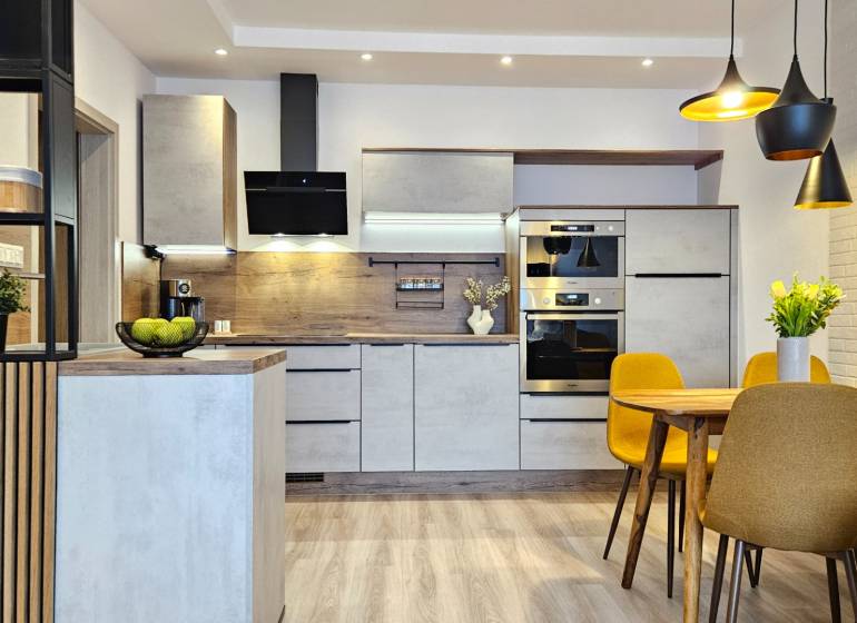 Küche in einer Einzimmerwohnung mit Holzboden, Esstisch und gelben Stühlen.