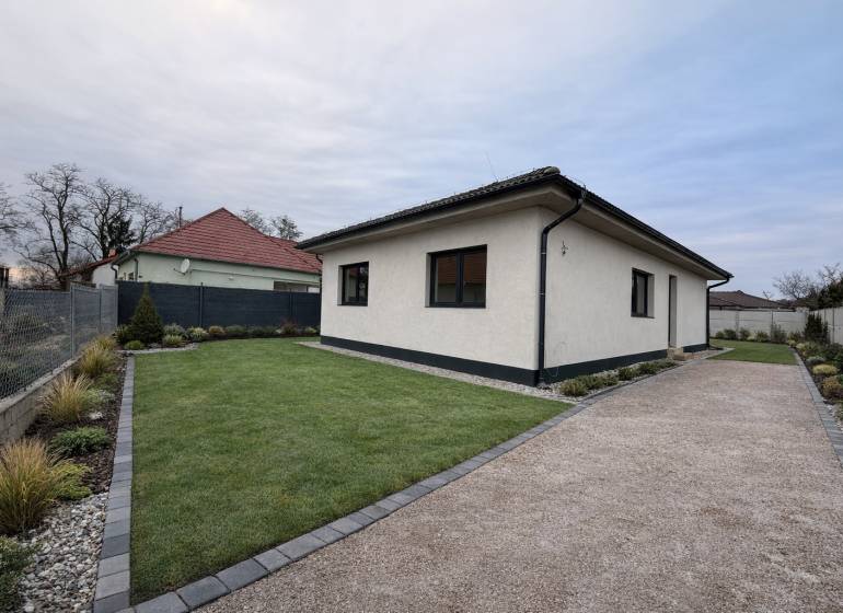 Ein Einfamilienhaus in Veľký Grob mit Rasen, einem Kiesweg und einem gepflegten Garten.