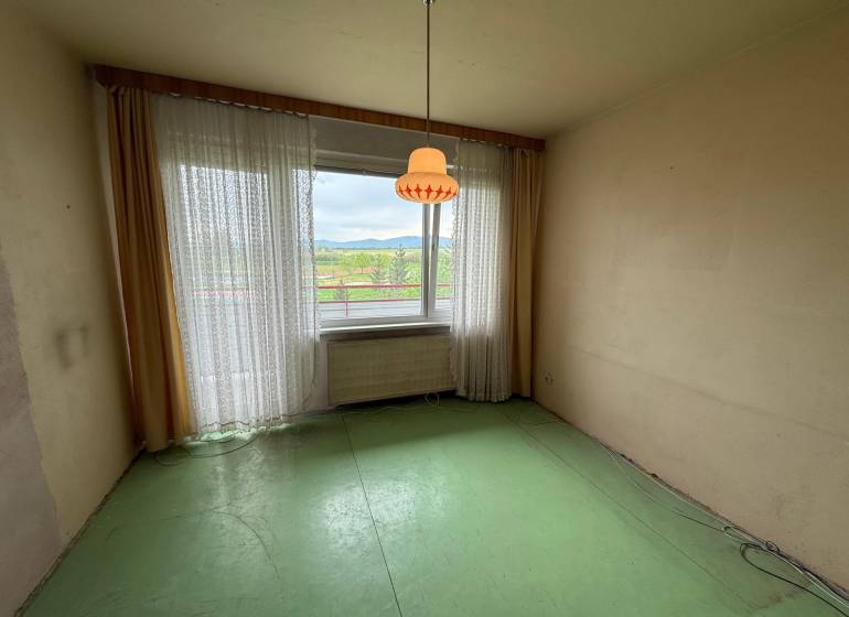Ein Zimmer mit grünem Boden und großem Fenster in einer 3-Zimmer-Wohnung.