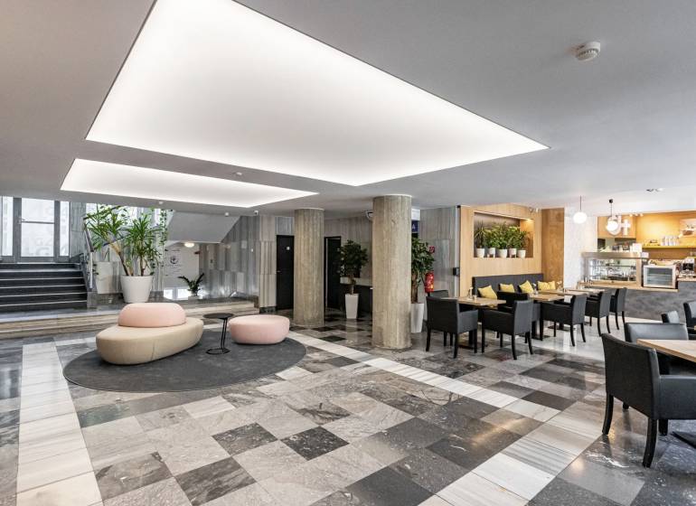 Büros mit schwarz-weißem Boden, Säulen, Sitzgelegenheiten und einem Café im Innenbereich.