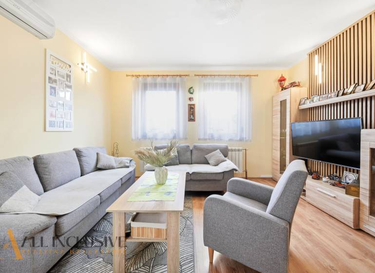 Wohnzimmer in einem Einfamilienhaus mit einem bequemen grauen Sofa und einem Boden in Holzoptik.