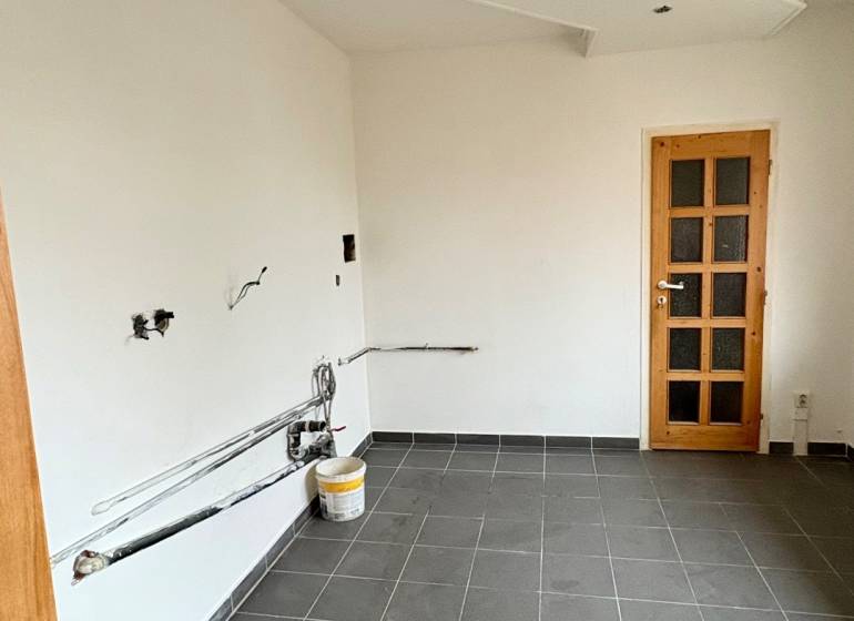 Ein leerer Raum in einer 2-Zimmer-Wohnung, dunkler Fliesenboden, weiße Wände, Holztüren.