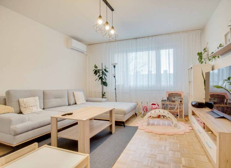 Helles Wohnzimmer in einer 3-Zimmer-Wohnung mit Holzboden und grauem Sofa.