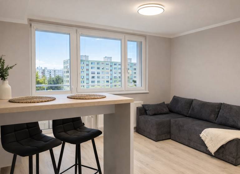 Obývací Zimmer in einer Zweizimmerwohnung mit Sofa, Bartisch und Stühlen.