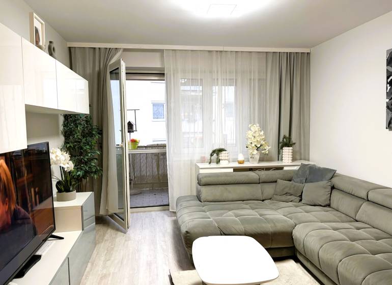 Wohnzimmer in einer 3-Zimmer-Wohnung mit einer bequemen Sofaecke und einem Boden in Holzoptik.