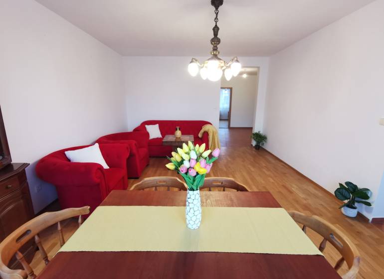 4-Zimmer-Wohnung mit roter Sitzgarnitur, Esstisch und Boden mit Holzdekor.