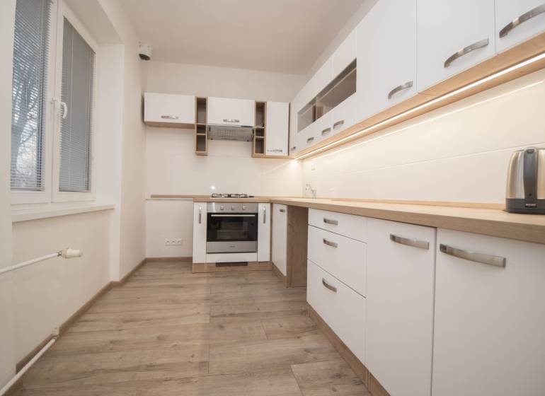 Küche mit Geräten, weißen Schränken und Holzboden in einer 2-Zimmer-Wohnung.