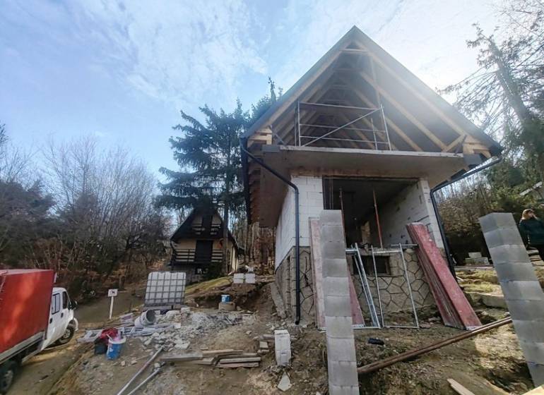 Eine Hütte im Bau auf Zajačia Debra in Holčíkovce, umgeben von Bäumen und Baumaterial.