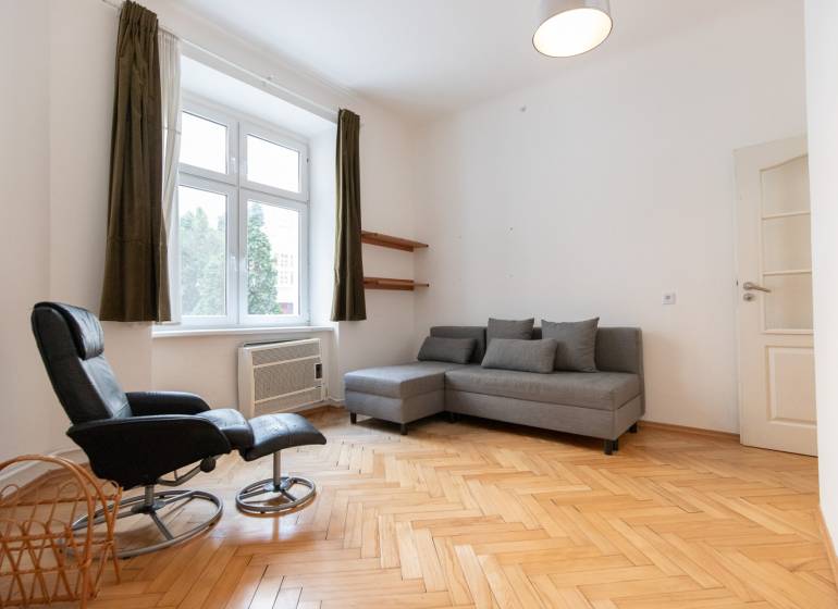 Helles Wohnzimmer mit Holzboden in einer 4-Zimmer-Wohnung, graues Sofa, Sessel.