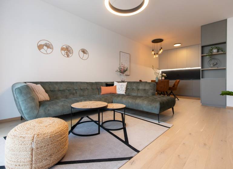 Wohnzimmer in einer Zweizimmerwohnung mit Sofa, Couchtischen und einem Boden in Holzoptik.