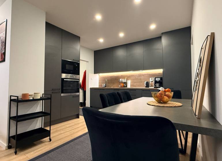 Küche in einer 4-Zimmer-Wohnung mit Holzboden, schwarzen Schränken und Esstisch.