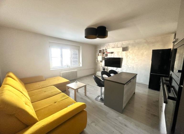 Wohnzimmer mit großem gelbem Sofa, Kücheninsel und Fernseher in einer 2-Zimmer-Wohnung.