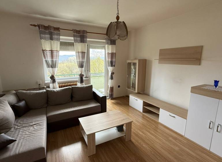 Wohnzimmer in einer 3-Zimmer-Wohnung mit einem bequemen Sofa, einem Boden in Holzoptik und einem Balkon.