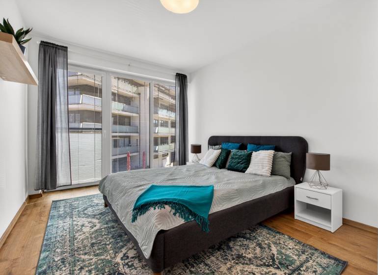 Schlafzimmer mit großem Bett, Balkontüren und Holzboden in einer 2-Zimmer-Wohnung.