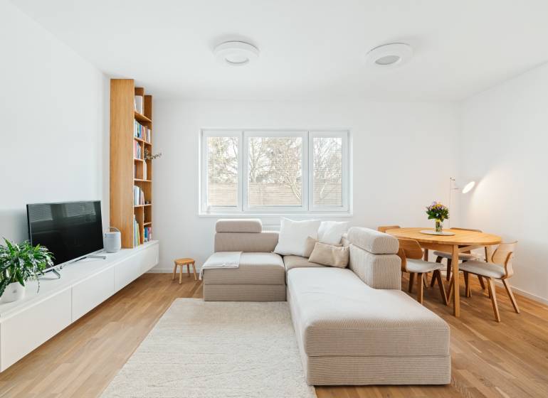 Wohnzimmer mit Sofa, Fernseher, Bücherregal und Esstisch, Boden mit Holzdekor.