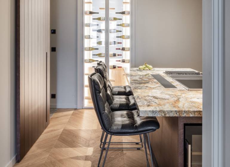 Küche in einer 4-Zimmer-Wohnung mit Bartresen, Stühlen und Boden mit Holzdekor.