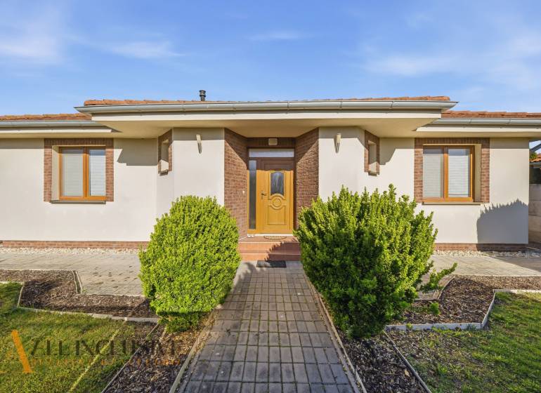 Ein Einfamilienhaus in Kútniky mit Strauchbepflanzung, weißer Fassade und braunen Akzenten.