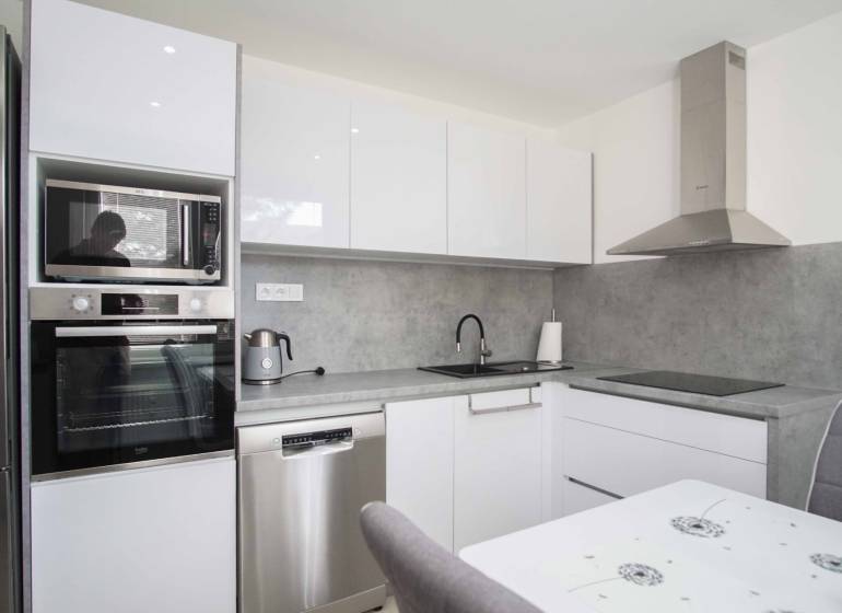 Moderne Küche mit weißen Schränken in einer 2-Zimmer-Wohnung, ausgestattet mit Geräten und Dunstabzugshaube.