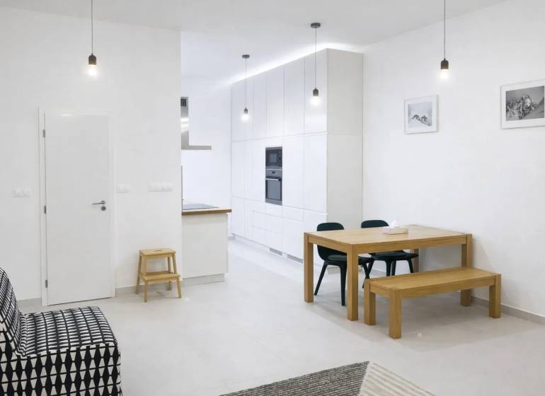 Innenraum einer 2-Zimmer-Wohnung mit weißen Wänden, einem Holztisch und einem schwarzen Sofa.