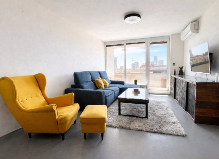 Wohnzimmer in einer 3-Zimmer-Wohnung mit gelbem Sessel, blauem Sofa und Fernseher an der Wand.