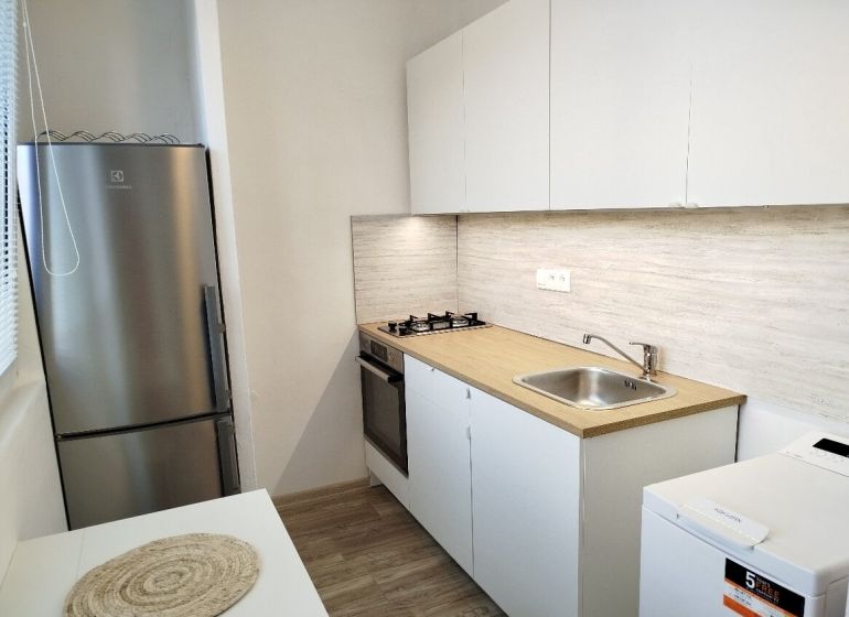 Küche in einer Einzimmerwohnung mit weißen Schränken, Kochfeld und Bodenbelag in Holzoptik.