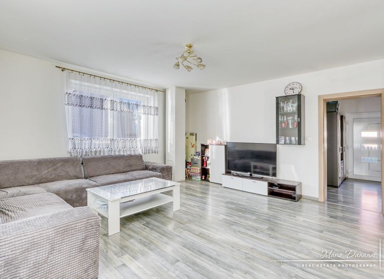 Wohnzimmer in einem Einfamilienhaus mit einer Eckcouch und einem Boden in Holzoptik.