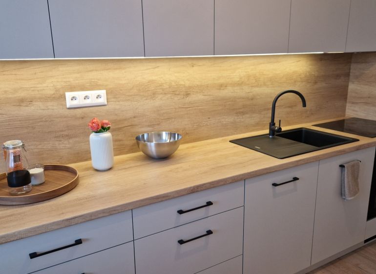 Küche in einer 3-Zimmer-Wohnung mit Holzboden, heller Küchenzeile und schwarzem Spülbecken.