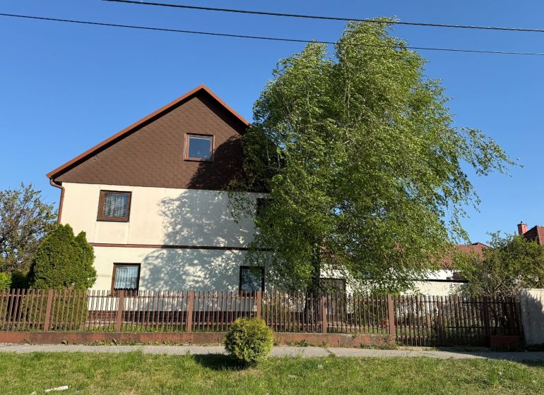 Ein Einfamilienhaus in Zlaté Moravce, ein Garten mit Bäumen, ein Zaun und blauer Himmel.