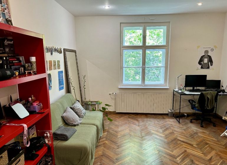 Wohnzimmer in einer 2-Zimmer-Wohnung mit Holzboden, Sofa und Computertisch.