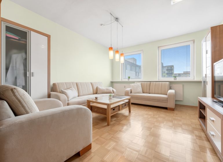 Wohnzimmer in einer 3-Zimmer-Wohnung mit einer Eckcouch und einem Boden in Holzoptik.