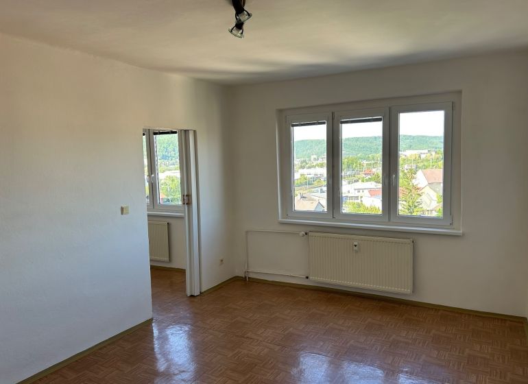 Helles Zimmer mit drei Fenstern und Holzboden in einer 2-Zimmer-Wohnung.