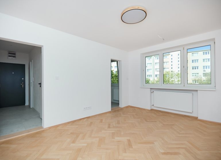 Eine Wohnung mit einem Holzboden, weißen Wänden und großen Fenstern.