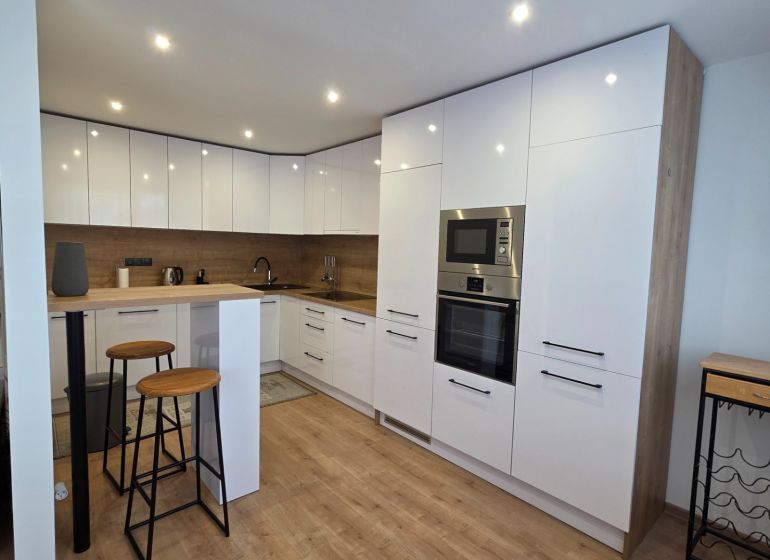 Küche in einer 3-Zimmer-Wohnung mit Bar-Sitzgelegenheiten und einem Boden in Holzoptik.