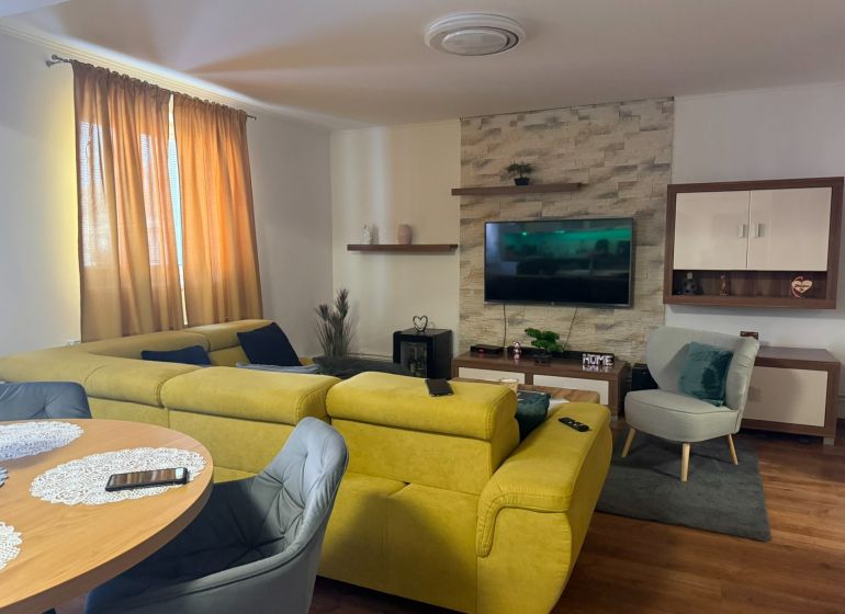 Wohnzimmer in einem Einfamilienhaus mit einem bequemen gelben Sofa und einem Boden in Holzoptik.