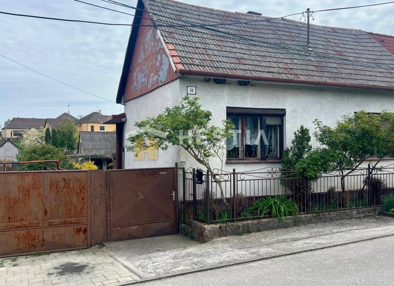Ein Einfamilienhaus in Cerová mit einem Tor und einem kleinen Garten, umgeben von Grün.