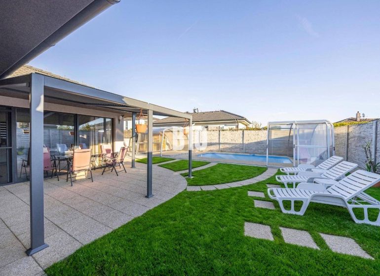 Ein Einfamilienhaus in Most pri Bratislave mit Terrasse, Pool und Liegestühlen auf dem Rasen.