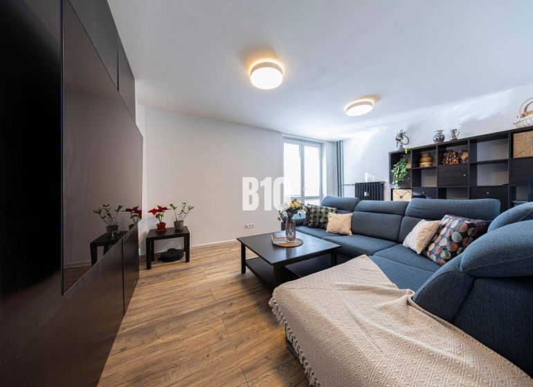 Wohnzimmer in einer 3-Zimmer-Wohnung mit einem blauen Sofa und einem Boden in Holzoptik.