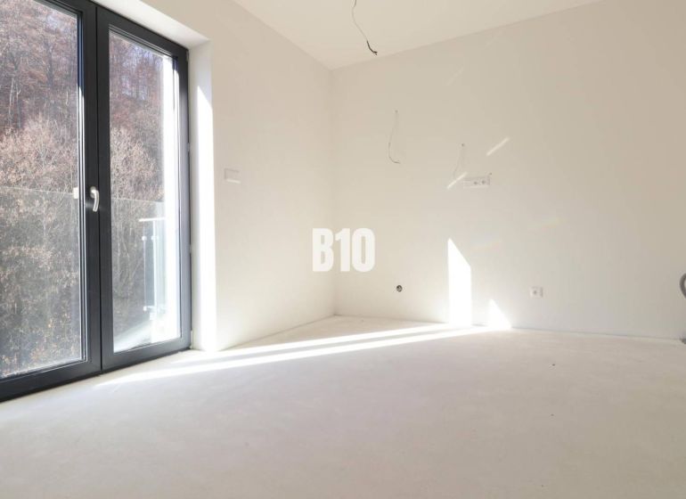 Ein leeres Zimmer in einer 3-Zimmer-Wohnung mit großen Fenstern und Blick auf die Natur.