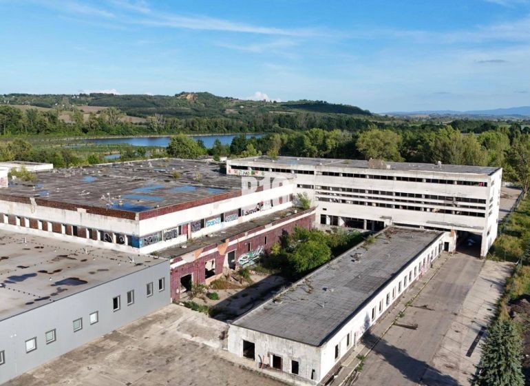Produktionsräume in Levice mit verlassenen Gebäuden, umgeben von Natur und einer Wasserfläche.