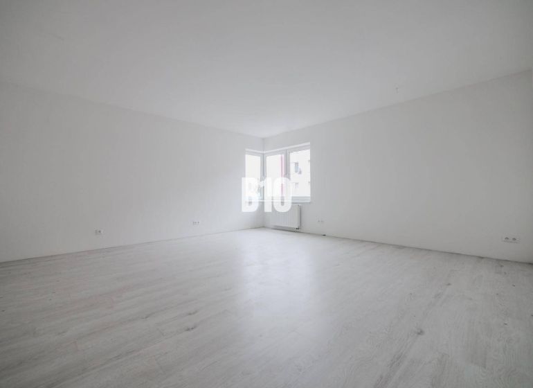 Ein geräumiges Zimmer mit weißen Wänden und einem großen Fenster in einer Einzimmerwohnung.