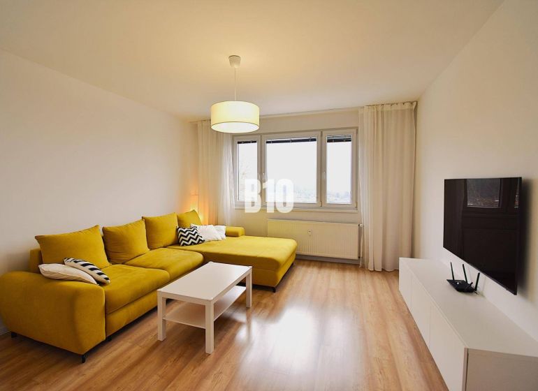 Wohnzimmer in einer 3-Zimmer-Wohnung mit einem markanten gelben Sofa und einem Boden in Holzoptik.