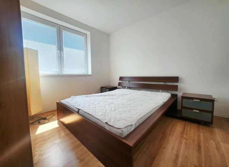 Ein Schlafzimmer mit Sonnenlicht, einem Bett, einem Nachttisch und einem Boden mit Holzdekor.