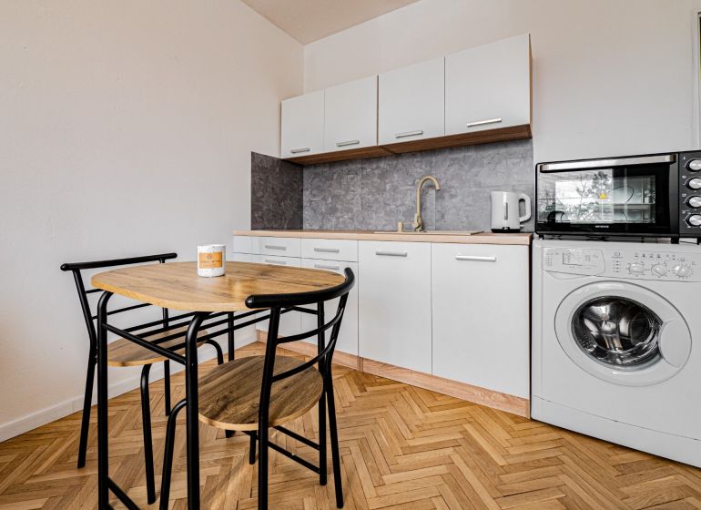 Einzimmerwohnung mit Küchenzeile und Geräten, Boden mit Holzdekor, Esstisch und Stühle.