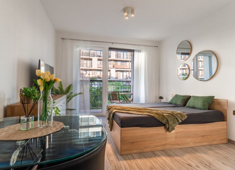 Helle 1-Zimmer-Wohnung mit Bett, Spiegeln und Holzboden, Balkon vor dem Fenster.